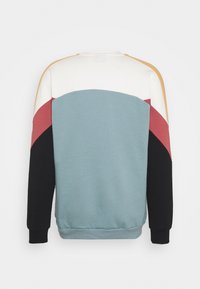 Kruhový svetr s barevnými bloky v světle modré, bílé, hořčicové, růžové a černé barvě, zobrazený ze zadní strany.