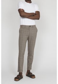 Ljusbruna rutiga byxor med slim fit och framfickor, bärs med en vit t-shirt och bruna sandaler, vilket visar en avslappnad stil.