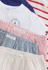 Cztery zestawy ubrań dla niemowląt z elastycznymi paskami w paski w kolorach czerwonym, niebieskim i beżowym, połączone z białymi i granatowymi bluzkami, jedna z nich z nadrukiem klubu żeglarskiego.