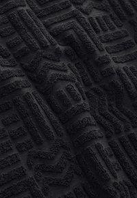 Texturerat svart tyg med upphöjda mönster av geometriska former och linjer, som visar en mjuk yta och mjuk textur.