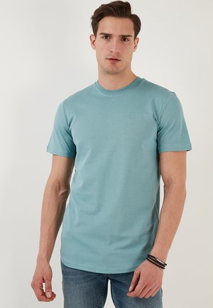 Tricou bleu deschis cu guler rotund, din bumbac moale, cu mâneci scurte și croială dreaptă, purtat cujeanși albaștri. Design simplu, fără modele.
