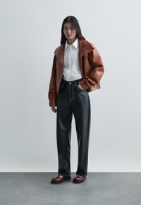 Καφέ δερμάτινο μπουφάν με φαρδιά γιακά, λευκό πουκάμισο με κουμπιά, σκούρο φαρδύ παντελόνι και μπορντό υποδήματα με χοντρές σόλες.