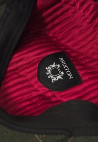 Black-lined, green fabric hat with a red corduroy interior. Features a label with the text "BRIXTON" and a crest design.