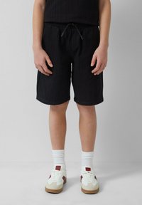 Zwarte, knielange shorts met een trekkoord in de taille, verticale strepen, gecombineerd met witte sokken en sneakers met rode accenten.