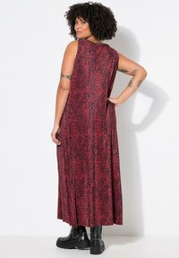 Ärmelloses Maxikleid in Rot mit schwarzem Tiermuster. Fließender Stoff reicht bis zu den Knöcheln und wird mit klobigen, schwarzen Nietenstiefeln kombiniert.