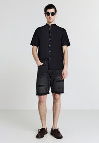 Black short-sleeve button-up shirt with a mandarin collar, paired with distressed black denim shorts and dark brown lace-up shoes.