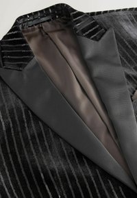 Black velvet blazer with sequined stripes, satin lapels, and a smooth inner lining. Features a sleek, tailored design.