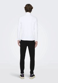 Camisa blanca de manga larga, pantalones negros y zapatillas negras con acentos morados. Corte relajado, tejido suave y diseño sencillo sin patrones.