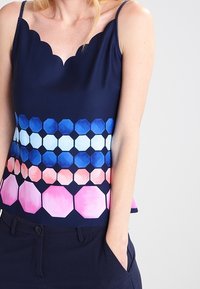 Námořnická top s krajkovým výstřihem; má hexagonální vzory v odstínech modré a růžové s přechody. Lehká tkanina, bez rukávů.