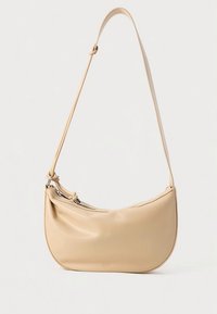 Sac à bandoulière en cuir beige avec une silhouette courbée, fermeture éclair et une seule sangle. Présente un design minimaliste avec un détail logo.