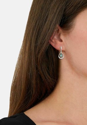 Boucles d'oreilles en argent en forme de goutte d'eau, ornées d'une gemme bleue entourée d'un fin cadre en argent, suspendues à un design en boucle. Texture lisse.