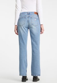 Jeans in denim azzurro chiaro con vestibilità dritta, vita media, cuciture in contrasto e tasche posteriori. Etichetta in pelle marrone sul retro.