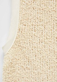 Jasno beżowy dziany materiał z luźnym, teksturowanym wzorem, wzdłuż krawędzi otoczony gładką, kremową tkaniną.