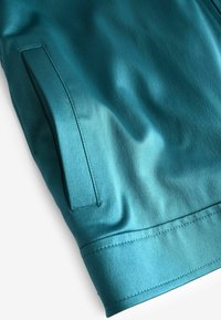 Teal satiin kangas sujuva tekstuuriga, küljetasku ja ühtlaselt õmmeldud äärtega all. Nähtav kõver kujundusdetail.