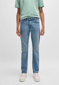 Jeans de perna reta azul-claro feitos de denim, com um leve efeito desbotado e design clássico de cinco bolsos. Usados com uma t-shirt verde e ténis.