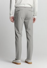 Lichtgrijze broeken met een slim fit, elastische tailleband en twee achterzakken. Gestyled met lichtgekleurde schoenen, weergegeven van de achterkant.