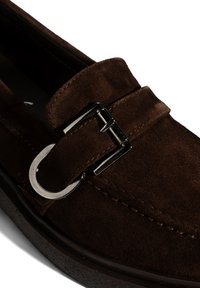 Braune Wildleder-Loafer mit einer dekorativen silbernen Schnalle, gepolstertem Kragen und strukturiertem Gummisohle, die die hochwertige Handwerkskunst hervorhebt.