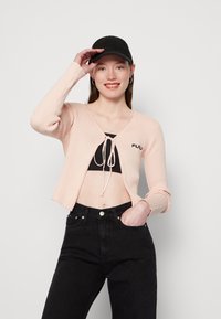 Heled roosa ribatatud kardigan, millel on sidumise detail, kantud musta lühikese toppi peale. Ühildatud kõrge vöökoha mustade teksadega.