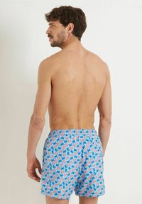 Costumi da bagno da uomo blu con motivo floreale in rosa e verde, vita elastica e tasche laterali, mostrati da dietro.