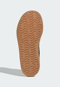 Crni potplat sportske tenisice s valovitom teksturom i gumiranim materijalom, sa središnjim logotipom i uzdignutim elementima za prianjanje.