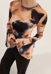 Langsleevetop in een mix van oranje, zwart en bruine abstracte patronen, met klokmouwen en een ronde halslijn.
