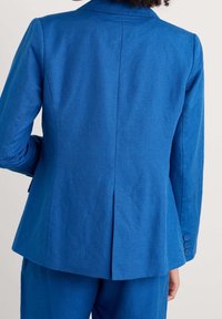 Blå blazer med texturerad yta, enda vent bak och fyra-knappränder. Skräddarsydd passform och skarpa slag.