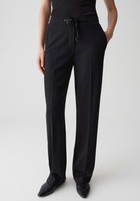 Pantaloni neri su misura con una vita regolabile, frontale piatto, tasche laterali e una texture liscia. Indossati con scarpe nere a punta.