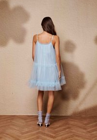 Svetlo modra obleka iz tila z večplastnimi volančki, tankimi nastavljivimi naramnicami in ohlapnim krojem. Kombinirana z sivimi ohlapnimi nogavicami in belimi salonarji.