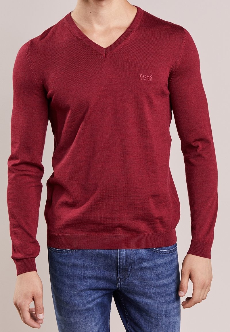 Röd långärmad v-neck tröja i finstickad kvalitet. Har en diskret logo på bröstet samt ribbade muddar och nederkant. Matchas med blå jeans.