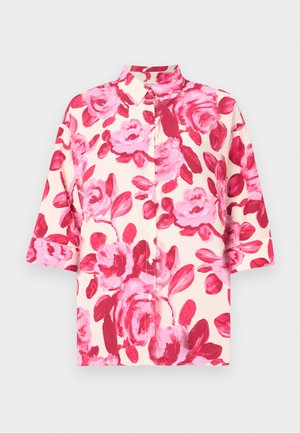 Camicetta a maniche corte con bottoni di colore crema, decorata con una grande stampa floreale rosa; presenta un colletto classico e una vestibilità rilassata. Il tessuto ha una consistenza liscia.