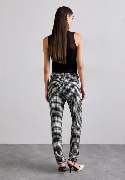 Musternahk, mustriseltikuga must ilma varrukateta tops, mis on ühendatud houndstooth mustriga pükstega. Pikk juuksed ja kõrged kontsad on nähtavad tagant.