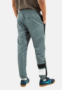 Grijze trainingsbroek met een gladde textuur, elastische tailleband, zijzakken en contrasterende zwart-witte panelen bij de onderbenen.