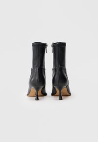 Botas de tobillo de cuero negro con tacón cónico, que cuentan con una cremallera trasera y una textura suave, diseñadas con un eje ajustado y sin patrones visibles.