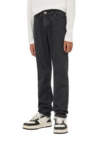 Jeans in denim nero con taglio dritto, cinque tasche e chiusura a bottone, abbinati a sneakers alte nere e bianche.