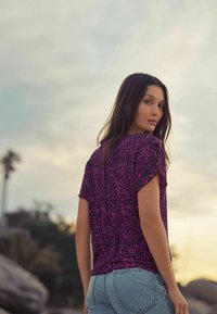 T-shirt à manches courtes de couleur rose vif avec un motif léopard, fabriqué en tissu léger ; associé à un short en denim bleu clair.