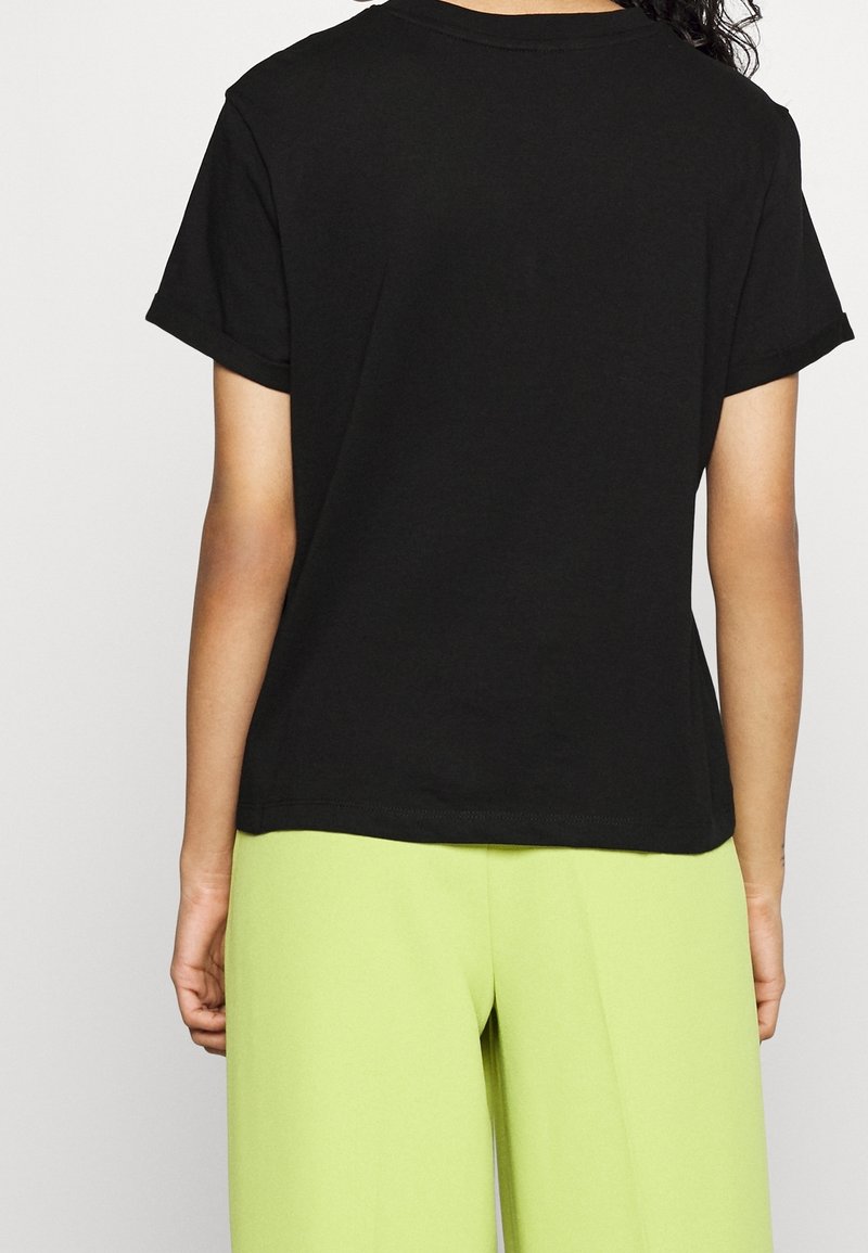 T-shirt en coton noir à manches courtes, coupe décontractée et revers roulés. Porté avec un pantalon taille haute vert vif.