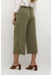 Olivgröna cropped byxor med en elastisk midja, med sidoklipp, i kombination med bruna klacksandaler. Slät textur.