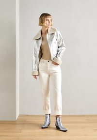 Chaqueta metálica plateada con cuello de piel, blusa beige, pantalones blancos con puños y botines plateados. Textura suave, diseño elegante.