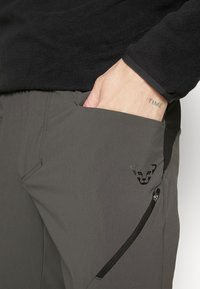 Gray pants made of lightweight fabric with a smooth texture. Features a black zipper pocket and a logo in the shape of a lion's head.