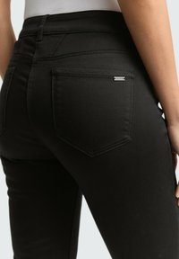 Zwarte denim jeans hebben een slim fit, achterzakken, subtiele stikseldetails en een klein merkteken op de rechterzak.