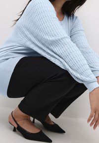 Jasnoniebieski sweter z teksturowanymi, prążkowanymi rękawami, w połączeniu z czarnymi dopasowanymi spodniami i czarnymi pantoflami na obcasie z zaostrzonym czubkiem.