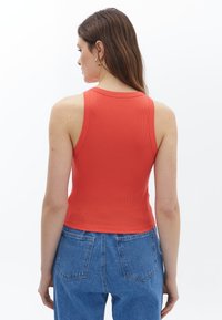 Červené žebrované tílko s přiléhavým střihem, kulatým výstřihem a zkráceným stylem, kombinované s džíny vysokého pasu v modré barvě.