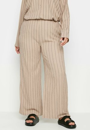 Beige wijde broek met verticale zwarte strepen, geribbelde textuur en een elastische tailleband. Gestyled met een bijpassende top en zwarte sandalen.