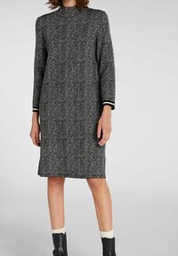 Robe à motif en chevrons noir et blanc avec des manches longues et un col haut, présentant des accents rayés noir et blanc aux poignets.