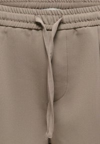 Pantalon décontracté beige avec une taille élastique et un cordon de serrage avant noué lâchement descendant au centre.