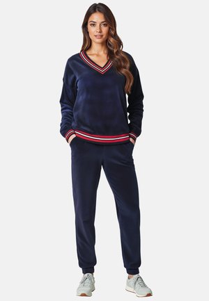 Navy-blue velour tracksuit featuring a V-neckline, multi-colored striped accents on cuffs and hem, and fitted jogger-style pants.