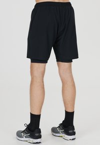 Mustat urheilushortsit, joissa on joustava vyötärö, sileä kangas ja rento leikkaus. Yhdistetty mustiin sukkiin ja harmaisiin urheilukenkään.