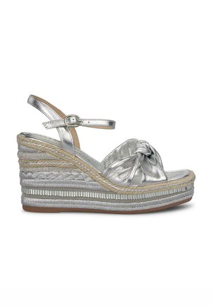 Sandali wedge argentati con design annodato, tomaia metallizzata, dettagli in juta intrecciata e bande di accento testurizzate. Fibbia regolabile alla caviglia.
