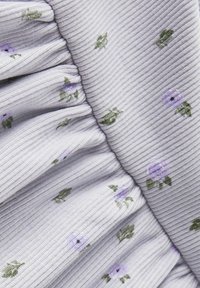 Raitakudetta vaaleanlaventelilla värillä, jossa on ripoteltuna pieniä purppuranvärisiä kukkakuoseja ja vihreitä lehtiä; sisältää kerättyä tekstuuria ja virtaavaa muotoilua.