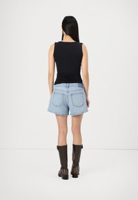 Top negro sin mangas, pantalones cortos de mezclilla azul claro y botas de cuero marrón hasta la rodilla con detalles de hebilla, vistas desde atrás.